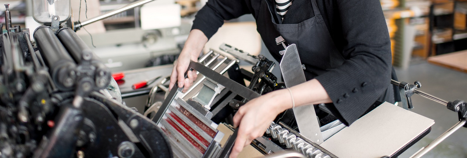 Female letterpress printer preparing print machine in workshop